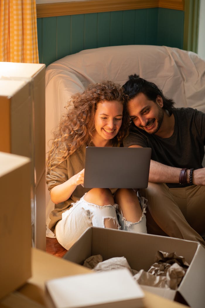 Home Smiling couple using laptop while unpacking boxes in their new home. Bright, cozy indoor setting perfect for relocation themes.